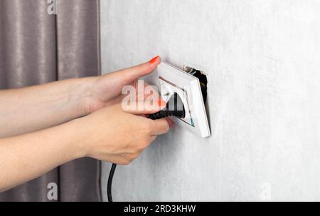 Das Mädchen zieht fälschlicherweise den Stecker aus der Steckdose und unterbricht die Steckdose. Stromschlaggefahr. Platz für Text kopieren Stockfoto
