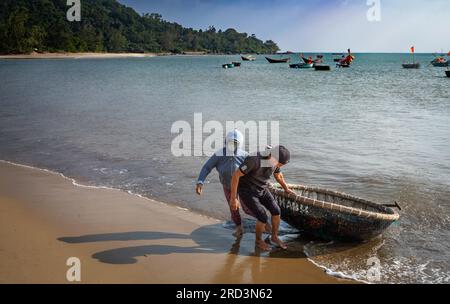 Ein vietnamesischer Mann und seine Frau kehren vom Angeln zurück und ziehen ihr traditionelles Korakel an Land in South Beach, Son Tra, Danang, Vietnam. Stockfoto