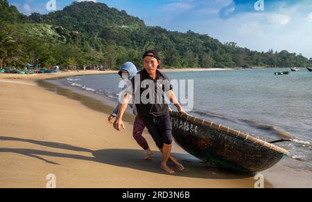 Ein vietnamesischer Mann und seine Frau kehren vom Angeln zurück und ziehen ihr traditionelles Korakel an Land in South Beach, Son Tra, Danang, Vietnam. Stockfoto