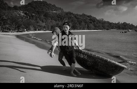 Ein vietnamesischer Mann und seine Frau kehren vom Angeln zurück und ziehen ihr traditionelles Korakel an Land in South Beach, Son Tra, Danang, Vietnam. Stockfoto