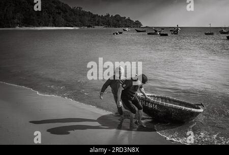 Ein vietnamesischer Mann und seine Frau kehren vom Angeln zurück und ziehen ihr traditionelles Korakel an Land in South Beach, Son Tra, Danang, Vietnam. Stockfoto