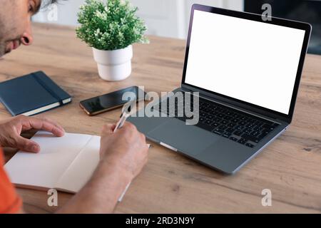 Ansicht vom Rücken eines Mannes, der ein Notebook benutzt und in ein Notebook schreibt. Modernes Büro. Modell-Laptop, Computer Stockfoto