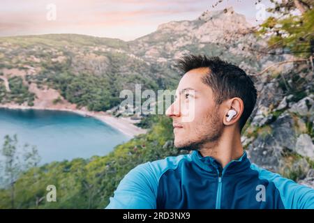 Der Mann wandert auf einem malerischen Pfad, taucht ein in die Schönheit der Natur, während er seine Lieblingsmusik über Kopfhörer genießt. Stockfoto