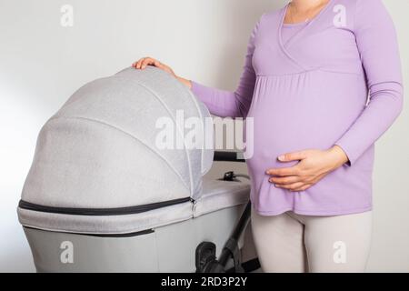 Ein schwangeres Mädchen mit einem großen Bauch wählt einen Kinderwagen für ihr ungeborenes Kind. Ich kaufe einen neuen Kinderwagen im Laden. Nahaufnahme Stockfoto