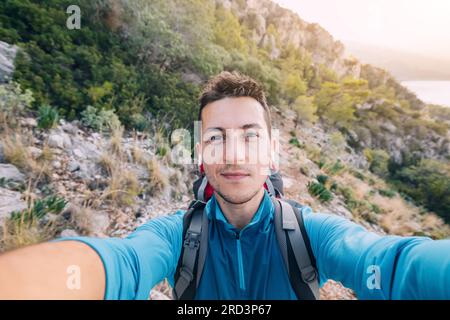 Der Mann wandert auf einem malerischen Pfad, taucht ein in die Schönheit der Natur, während er seine Lieblingsmusik über Kopfhörer genießt. Stockfoto