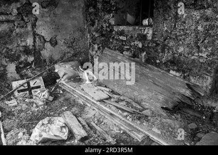 Ein zerstörtes Steingebäude voller Bauschutt und Müll, einschließlich Holztür mit festem Kreuz. Schwarzweißbild. Stockfoto