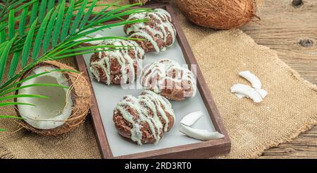 Profiteroles wählen Gebäck mit Kokosnusscreme in tropischem Stil. Palmenblätter, süßes gesundes Dessert, flach liegend, Bannerformat Stockfoto