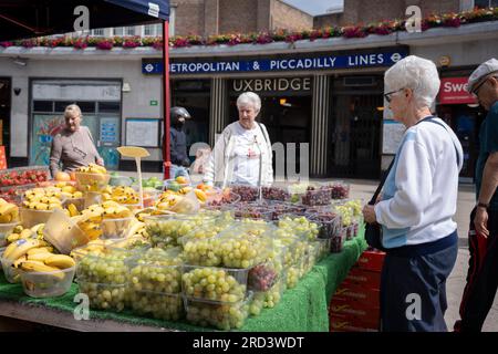 Zwei Tage vor der politischen Nachwahl kaufen die Bewohner Obst und Gemüse vor der U-Bahn-Station Uxbridge am 18. Juli 2023 in London, England. Der Wahlkreis Uxbridge und South Ruislip ist eine von drei lokalen Nachwahlen, die am selben Tag stattfinden, aber Uxbridge war im parlament acht Jahre lang durch den ehemaligen konservativen Premierminister Boris Johnson vertreten, bevor er als Abgeordneter zurücktrat. Am 20. Juli werden 17 Kandidaten dagegen antreten. Stockfoto