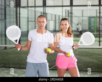 Paar mit Padel-Schlägern, die auf dem Tennisplatz posieren Stockfoto