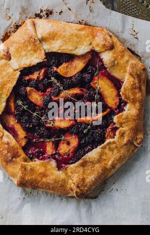 Direkt über hausgemachter Brombeeren-, Pfirsich-, Thymian-Galette auf Pergamentpapier Stockfoto