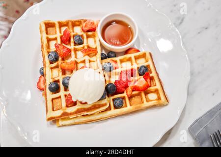 Klassische Wiener Waffeln mit Eis, Beeren und Ahornsirup. Frühstück im Café. Tisch im Restaurant. Stockfoto