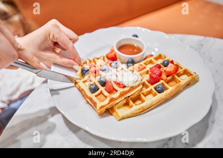 Klassische Wiener Waffeln mit Eis, Beeren und Ahornsirup. Frühstück im Café. Tisch im Restaurant. Stockfoto