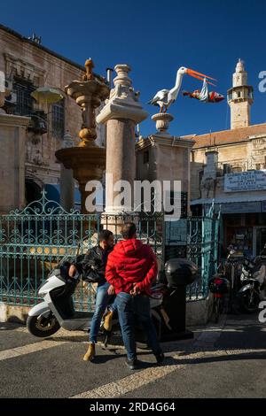 Vertikaler Blick auf zwei Männer, die sich vor dem Muristan-Brunnen im christlichen Viertel der Altstadt von Jerusalem, Israel, entspannen Stockfoto