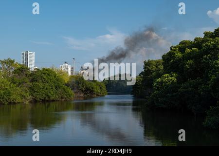 Calm River überquert den Mangrovenpark in Cartagena de Indias, Kolumbien, mit dunklem Rauch, der bei Sonnenuntergang von den weißen Gebäuden kommt Stockfoto