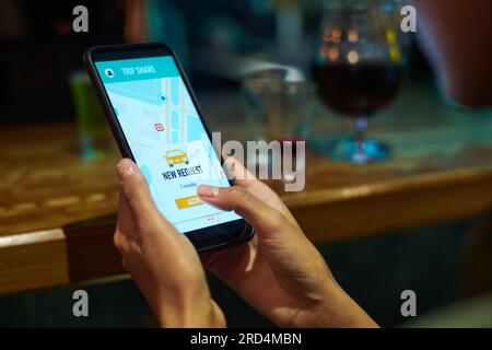 Hände einer jungen Frau, die ein Taxi mit einer mobilen App bestellt, während sie in der Bar sitzt und die Schaltfläche „Annehmen“ auf dem Smartphone berührt Stockfoto