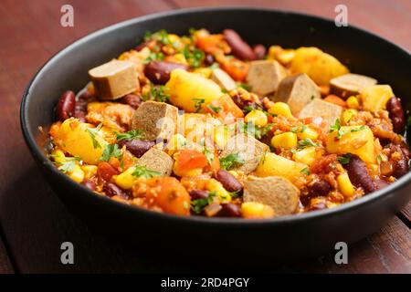 Veganer Cowboy-Eintopf mit Zwiebeln, Paprika, TVP-Granulat, zerdrückten Tomaten, Kidnierenbohnen, Kartoffeln, Mais und vegane Hotdog-Stücke Stockfoto