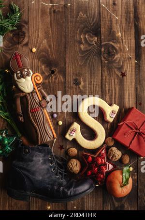 Nikolausschokolade mit Geschenken in der Nähe des Kinderstiefels mit Karotten auf Holzhintergrund Stockfoto