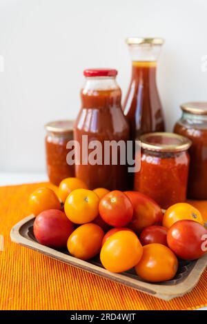 Das Verfahren zur Konservierung eingelegter Tomaten und Paprika in Glasgefäßen auf dem Tisch. Adjika, würzig-süße vegetarische Sauce zum Essen Stockfoto