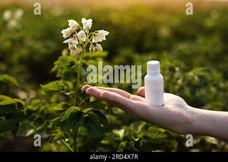 Probleme und Lösung der Gartensaison. Zugeschnittene Fotohand des Bauern hält weiße Flasche mit Modell für Gift, Pestizidflüssigkeit von Pflanzenkrankheiten und Stockfoto
