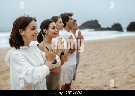 Gruppe junger Frauen und Männer, die während ihres Morgenübens am Strand am Meer meditieren, freier Raum Stockfoto