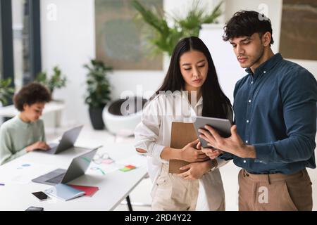 Seriöse Japanische Geschäftsfrau Und Arabischer Geschäftsmann, Der Mit Einem Tablet Im Innenbereich Arbeitet Stockfoto
