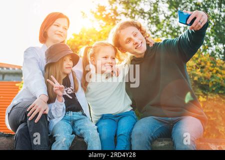 Porträts von drei lächelnden Schwestern und einem Bruder des Teenagers, der mit einer modernen Smartphone-Kamera Selfie-Portraits aufnahm. Sorglos glücklich jungen Teenholz, Kindheit Stockfoto