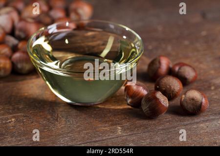 Haselnussöl in einer kleinen Glasschüssel und ganze Haselnüsse Stockfoto