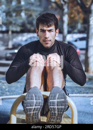 Vorderansicht eines jungen Mannes, der Bauchübungen an einem öffentlichen Gerät im Outdoor-Fitness macht Stockfoto