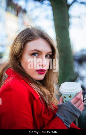 Porträt einer jungen Frau, die im Winter Kaffee trinkt und auf einer Bank sitzt Stockfoto