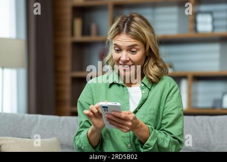 Fröhliche ältere Frau zu Hause, die lächelt und auf dem Sofa sitzt, im Wohnzimmer telefoniert, online-Seiten durchsucht und eine Nachricht anruft. Stockfoto