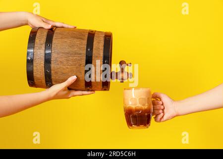 Frau, die Bier aus dem Fass in einen Becher auf gelbem Hintergrund gießt Stockfoto