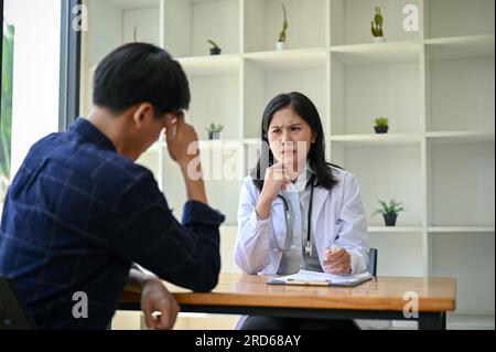 Eine gestresste und ernsthafte asiatische Ärztin hat ein ernstes Treffen mit einer Patientin in ihrem Untersuchungsraum in einem Krankenhaus. Stockfoto