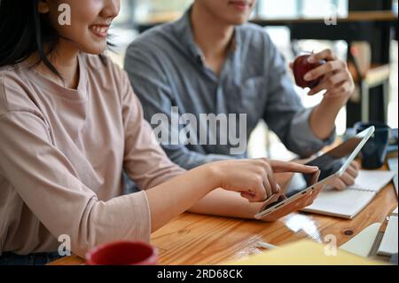 Nahaufnahme von zwei glücklichen jungen asiatischen Studenten, die zusammen auf einen Tablet-Bildschirm schauen, sprechen und ihre Ideen für ein gemeinsames Projekt teilen Stockfoto