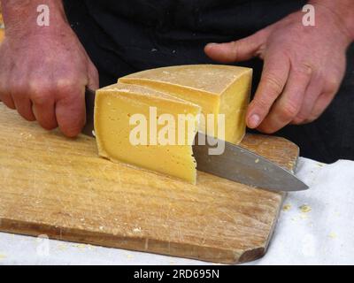 Tasmanischer Marktständer und Käsehersteller, der einen Käse im Cheddar-Stil für einen Kunden aufschneidet Stockfoto