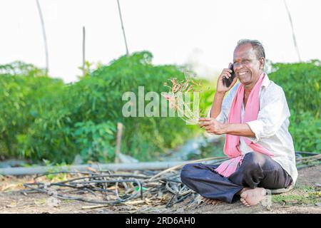 Glücklicher Bauer, der im Boden sitzt und telefoniert, alter indischer Bauer Stockfoto