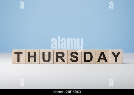 Text Donnerstag über Holzwürfel auf blauem Hintergrund. Wochentag auf Holzblöcken. Webbanner für Wochentage. Ursprünglicher Kalender. Teil der Serie. Zeitkonzept Stockfoto