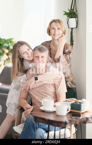 Porträt lächelnde Erwachsene Tochter umarmte älteren Vater von hinten, schaute in die Kamera, zwei Generationen, wunderschöne junge Frau umarmte einen erwachsenen Mann, posierte für ein Foto mit Eltern Stockfoto