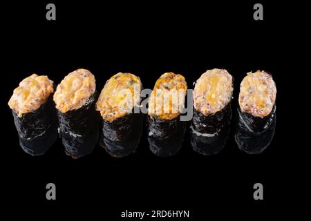 Gebackenes Maki-Sushi. Heiße Unagi Maki mit Tobiko. Sushi-Brötchen mit gebackenem Käse, Masago und Unagi-Sauce auf schwarzem Hintergrund mit Reflektio Stockfoto