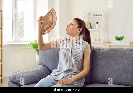 Gestresste, müde Frau, die einen Ventilator benutzt und an Hitze leidet, Sommer hohe Temperaturen zu Hause. Stockfoto