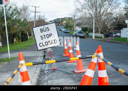 BUSHALTESTELLE GESCHLOSSEN Schild zwischen orangefarbenen Verkehrskegeln an der Bushaltestelle. Nicht wiedererkennbare Autos und Menschen auf der Straße. Reparatur von durch Hochwasser beschädigten Straßen in Auckla Stockfoto