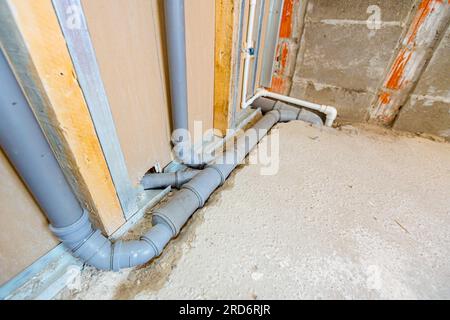 Neue Wasserinstallation, freiliegende graue PVC-Abwasserrohre an der Gipskartonwand montiert. Stockfoto