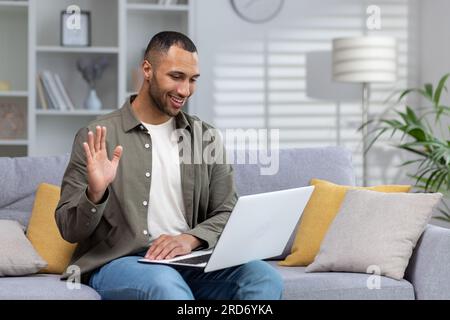 Glücklicher und lächelnder junger spanischer Mann, der aus der Ferne mit seinem Psychologen spricht, Hand in die Kamera winkt, sich geistig wohl fühlt. Stockfoto