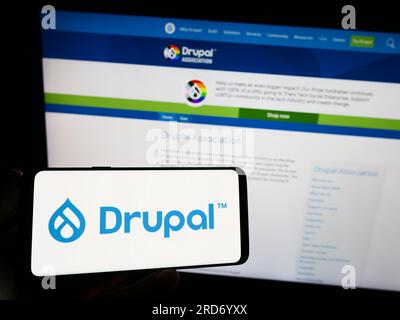 Person, die ein Smartphone mit dem Logo des Content-Management-Systems Drupal auf dem Bildschirm vor der Website hält. Konzentrieren Sie sich auf das Display des Telefons. Stockfoto