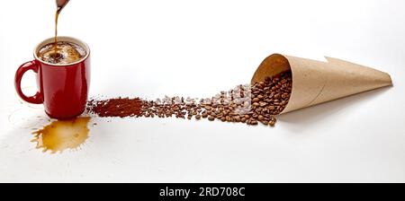 Roter Becher mit ausgegießtem Kaffee und Spritzer und handgefertigte Papiertüte mit verstreuten Körnern gemahlenen und zerstoßenen Kaffees. Zubereitungskonzept für Kaffeegetränke Stockfoto