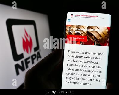 Person, die ein Mobiltelefon mit einer Webseite der National Fire Protection Association (NFPA) auf dem Bildschirm vor dem Logo hält. Konzentrieren Sie sich auf die Mitte des Telefondisplays. Stockfoto