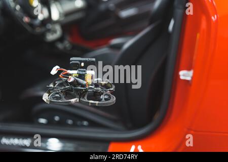 Die FPV-Drohne fliegt in der Nähe eines roten Autos in der Werkstatt. Hochwertiges Foto Stockfoto