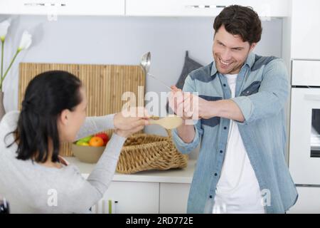 Komisches Paar, das sich in der Küche mit Utensilien streitet Stockfoto