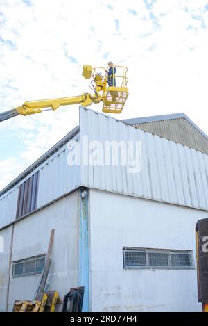 Frau im Kirschpflücker-Korb über dem Industriegebäude Stockfoto