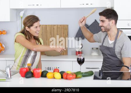 Komisches Paar, das beim Kochen so tut, als würde es sich mit Utensilien streiten Stockfoto