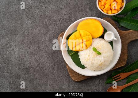 Köstlicher klebriger Reis aus thailändischer Mango mit geschnittenen frischen Mangofrüchten auf einem Teller mit grauem Tischhintergrund. Stockfoto